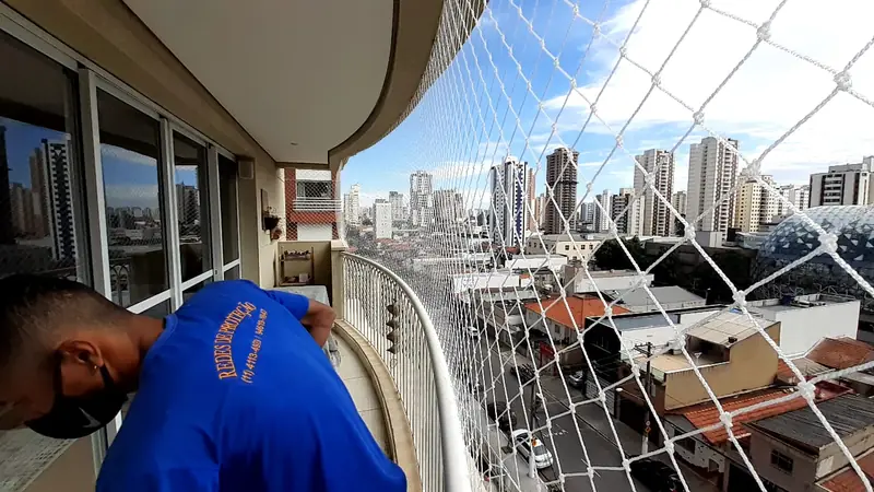 Instalador da Elite Redes fixando rede de proteção em sacada com vista para a cidade