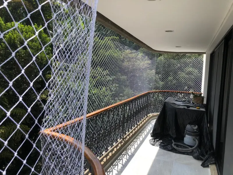 Rede de proteção instalada em varanda com guarda-corpo de ferro e vista para as árvores